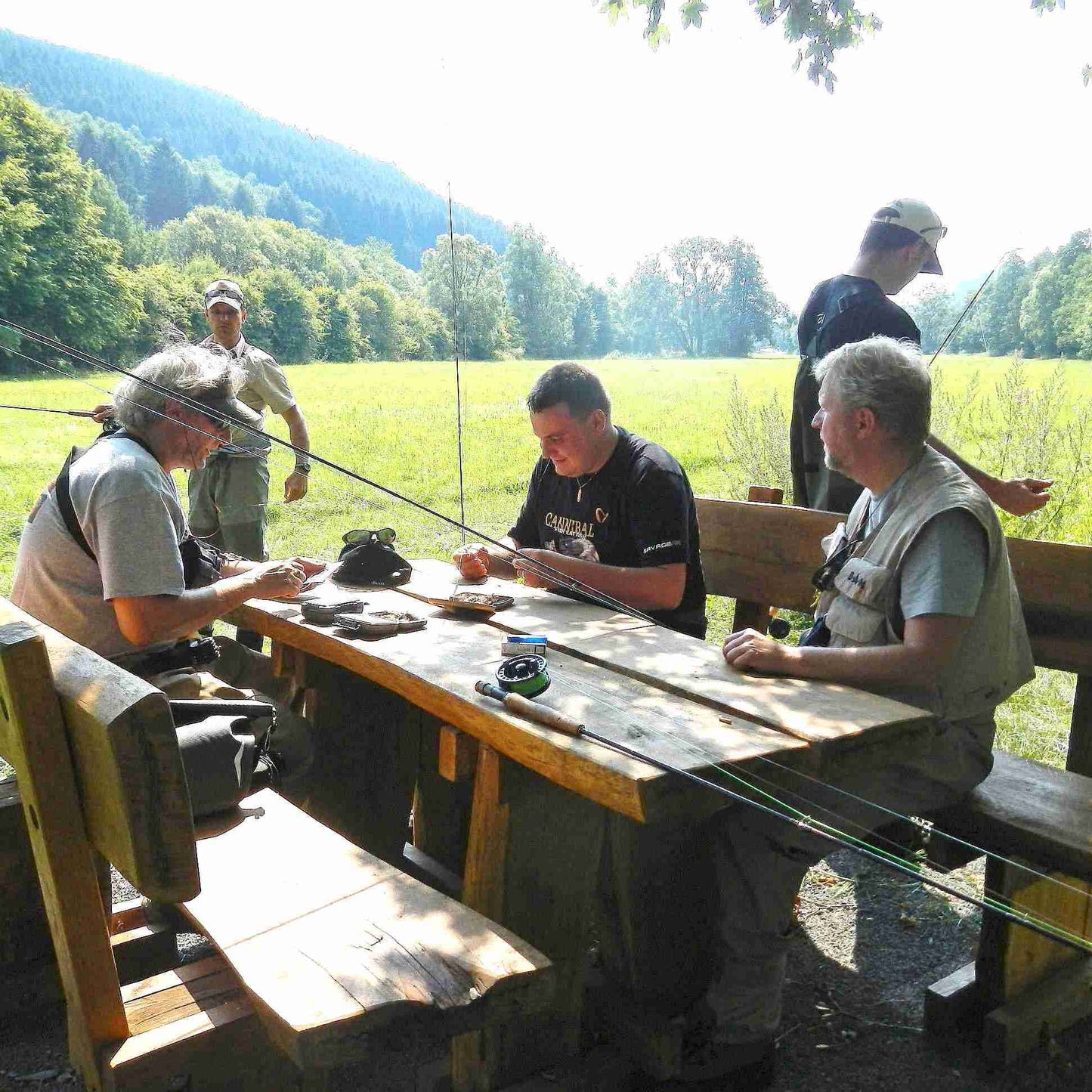 zu sehen sind 5 Fliegenfischer auf einer Holzbank mit Tisch