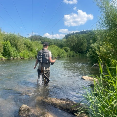 zu sehen ist ein Fliegenfischer von hinten durch den Bach watend