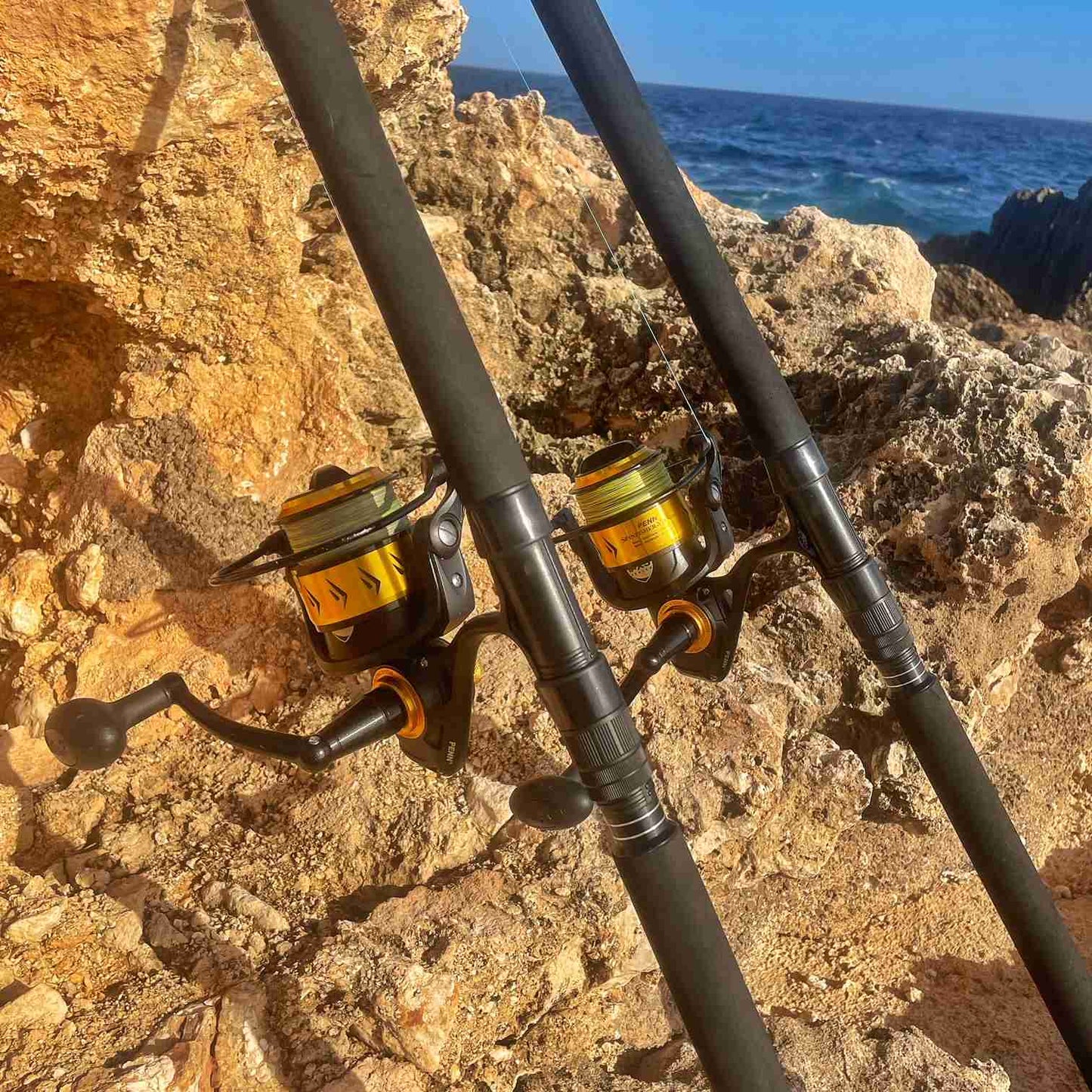 zu sehen sind 2 Angelruten, die am Felsen lehnen. Im Hintergrund ist das Meer.